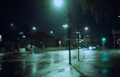 an empty city street at night with lights on and rain all over the road surface