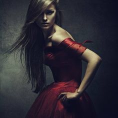 a woman in a red dress is posing for a photo with her long hair blowing in the wind