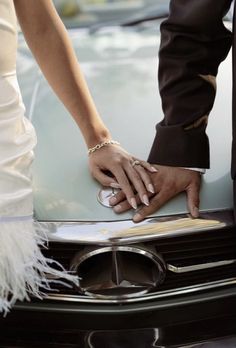 a bride and groom holding hands on the hood of a car with feathers around it