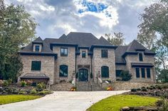 a large brick house sitting on top of a lush green field next to a forest