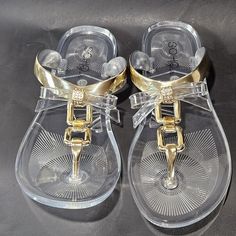 These Flat Clear Sandals Are Perfect For Warm Weather And Boast Cute Golden Bows And T Strap Style Closure Gold Jelly Sandals With Round Toe For Spring, Gold Flat Jelly Sandals For Summer, Casual Gold Flip Flops For Parties, Gold Trendy Synthetic Flip Flops, Trendy Gold Synthetic Flip Flops, Gold Open Toe Jelly Sandals For Vacation, Gold Jelly Sandals For Summer Beach, Trendy Gold Sandals For The Beach, Gold Jelly Sandals For Beach And Spring