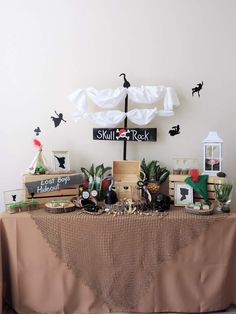 a table topped with lots of fake plants and books under an umbrella that says skull's rock