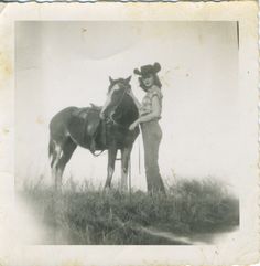 an old black and white photo of a woman standing next to a horse in a field