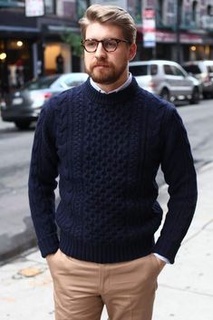 a man wearing glasses and a sweater is standing on the sidewalk