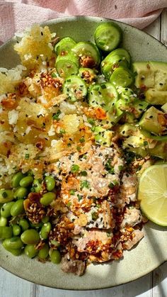 a white plate topped with meat, vegetables and rice next to a slice of lime