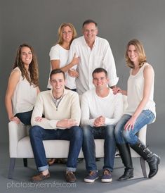 a group of people sitting on top of a white couch in front of a gray wall