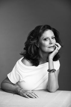 a black and white photo of a woman sitting at a table with her hand on her chin