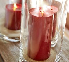 two red candles sitting in glass vases on a wooden table next to each other