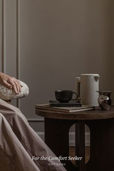 a person laying in bed next to a table with a coffee cup on top of it