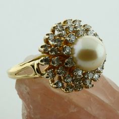 14K Yellow gold Large White Pearl and 1.2ct estimate Diamond Halo Ring, 8mm pearl center, 3 rows of tiered diamonds G color SI1 clarity, .75 inch across, sits 5/8 inch off finger, open work half shank, split shank, Ring size 6, Circa 1970, 10.5 grams Stock # BB258R11 This listing contains photographs of the actual item you will receive. Our items are in excellent condition with little or no signs of wear and many are one of a kind pre-owned estate finds. Please look closely at the pictures in th Gold Brilliant Cut Pearl Ring For Formal Occasions, Gold Pearl Ring With Brilliant Cut For Formal Occasions, Formal Gold Pearl Ring With Brilliant Cut, Gold Cluster Pearl Ring For Formal Occasions, Gemstone Rings Vintage, Diamond Pendants Designs, Split Shank Ring, Diamond Halo Ring, Diamond Collection