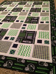 a green and white quilt on the floor with black and white squares, football helmets, and chevrons