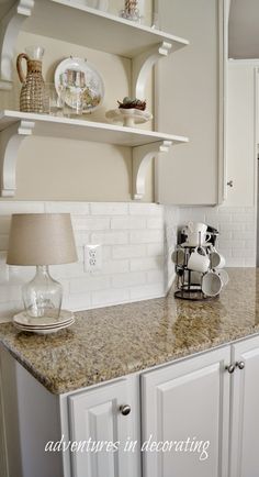 a kitchen with white cabinets and marble counter tops, an open shelving above the sink