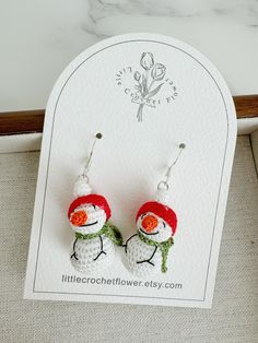 two little snowmen wearing red hats and green scarfs are sitting on a card