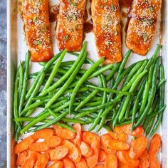 salmon, green beans and carrots are arranged on a baking sheet with seasoning