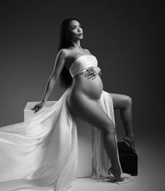 a pregnant woman in a white dress poses for a black and white photo with her legs spread out