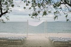 an empty beach with white chairs and a canopy