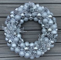 a wreath with silver and silver ornaments hanging from it's sides on a wooden wall