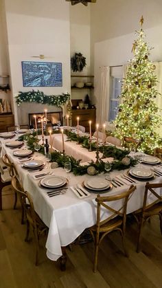 a dining room table set for christmas dinner with candles and greenery on the table