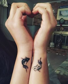 two people with tattoos on their arms holding hands in the shape of heart and fish