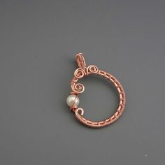 a copper wire and pearl pendant on a gray surface with a white bead in the middle