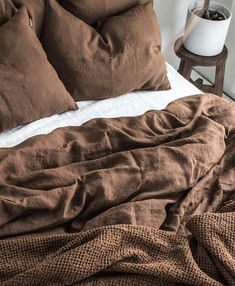 an unmade bed with brown linens and pillows on top of it, next to a night stand