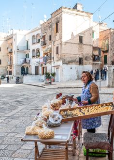 a woman standing next to a table filled with food on top of a stone street