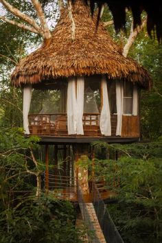 a tree house in the middle of trees with white curtains on it's windows