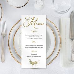 a table setting with white and gold plates, silverware and menu cards on it