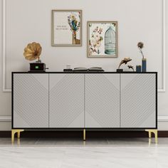 a white and black sideboard with two pictures on the wall above it next to a gold birdcage