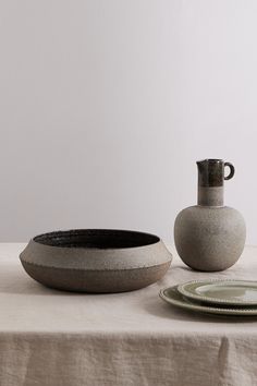 a table topped with a vase and plate next to a bowl on top of a table