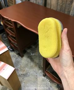 a person holding a sponge in front of a wooden desk with drawers and other furniture