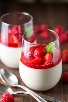 two glasses filled with yogurt and strawberries next to some raspberries