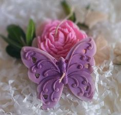 a purple butterfly sitting next to a pink flower on top of white shredded paper with green leaves