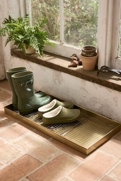 two pairs of rain boots sitting on top of a grate in front of a window