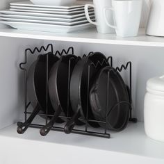 black pots and pans are hanging on a rack in front of white plates, cups and utensils