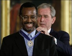 a man in a suit and tie smiles as he adjusts his medal