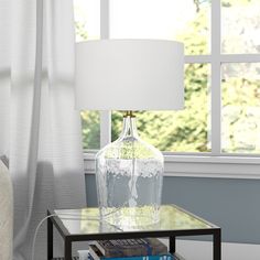 a table with a lamp and books on it in front of a window, next to a couch