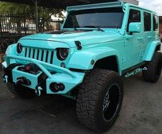 a light blue jeep parked in front of a metal structure with black tires and rims