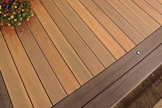 a brown wooden deck with flowers in the center and a potted plant behind it