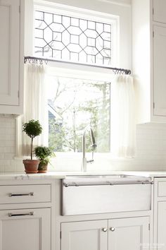 a kitchen with white cabinets and a window above the sink that has a potted plant in it