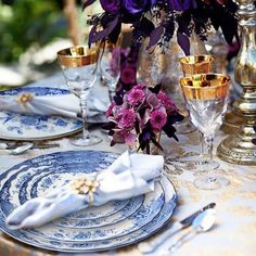 the table is set with blue and white plates, silverware, and purple flowers