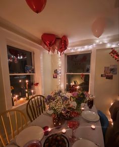 a dining room table with plates and bowls on it, candles in the window behind