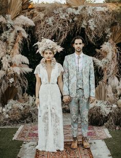 a man and woman standing next to each other on top of a rug in front of trees