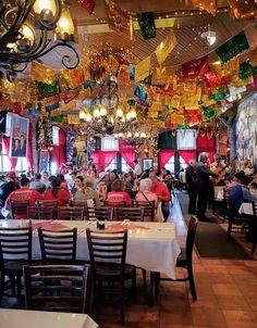 many people are sitting at tables in a restaurant with chandeliers hanging from the ceiling