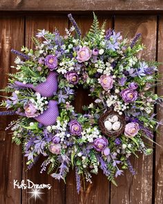 a wreath with purple and white flowers hanging on a wooden wall next to a bird's nest