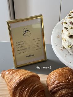 two croissants sitting on a table next to a plate with a pastry