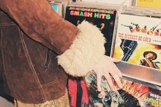 a person with their hand on a pile of cds in front of a wall full of dvds