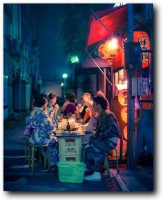 group of people sitting around a table in the middle of an alleyway at night