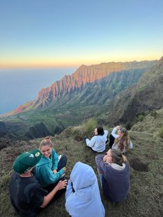 four people sitting on the side of a mountain looking out at the ocean and mountains