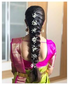 a woman with long hair wearing a pink and green saree, braided into a ponytail